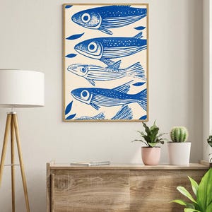 May include: A framed print of a blue and white illustration of five fish swimming in a row. The fish are stylized and have a simple design. The background is a light cream color.