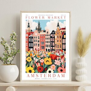 May include: A colorful poster with a whimsical illustration of a flower market in Amsterdam. The poster features a row of colorful buildings with red roofs and a field of flowers in the foreground. The text on the poster reads "Flower Market" and "Amsterdam".