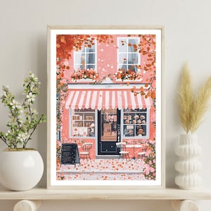 May include: A pink storefront with a white awning and striped canopy. The shop has a black door and windows with pastries displayed inside. There are two tables and chairs outside with pink flowers and leaves on the ground.