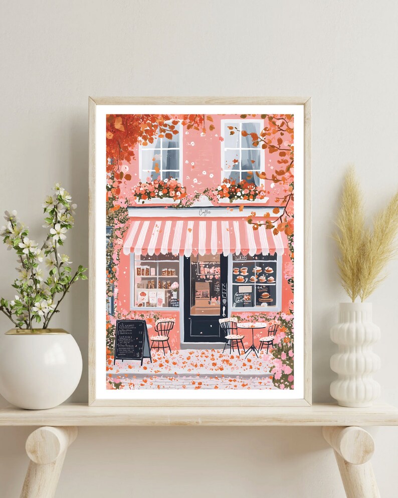 May include: A pink storefront with a white awning and striped canopy. The shop has a black door and windows with pastries displayed inside. There are two tables and chairs outside with pink flowers and leaves on the ground.