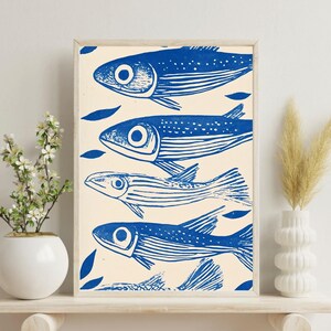 May include: A framed print of a blue and white illustration of four fish swimming in a row. The fish are stylized and have a simple design. The background is a light cream color.