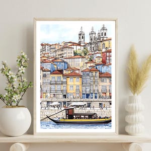 May include: A watercolor painting of a cityscape with colorful buildings and a boat on the water. The buildings are clustered together and have a variety of architectural styles. The boat is a traditional Portuguese boat with a yellow stripe and a brown hull.