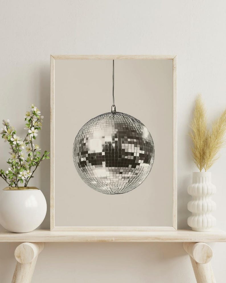 May include: A framed print of a silver disco ball hanging from the ceiling against a beige background.