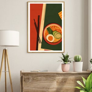 May include: A framed illustration of a bowl of ramen with chopsticks, a green onion, a boiled egg, and a slice of cucumber. The background is a red, green, and yellow abstract design.