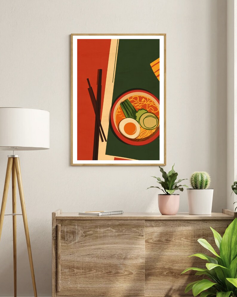 May include: A framed illustration of a bowl of ramen with chopsticks, a green onion, a boiled egg, and a slice of cucumber. The background is a red, green, and yellow abstract design.