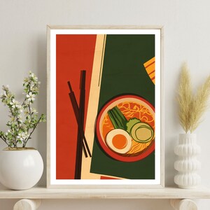 May include: A framed illustration of a bowl of ramen with chopsticks, egg, green onions, and a slice of cucumber. The background is a red and green colour scheme.