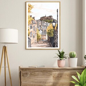 May include: A watercolour painting of a street in Edinburgh, Scotland. The street is lined with buildings and there is a castle in the background. The street is cobbled and there is a lamppost on the right side of the image.