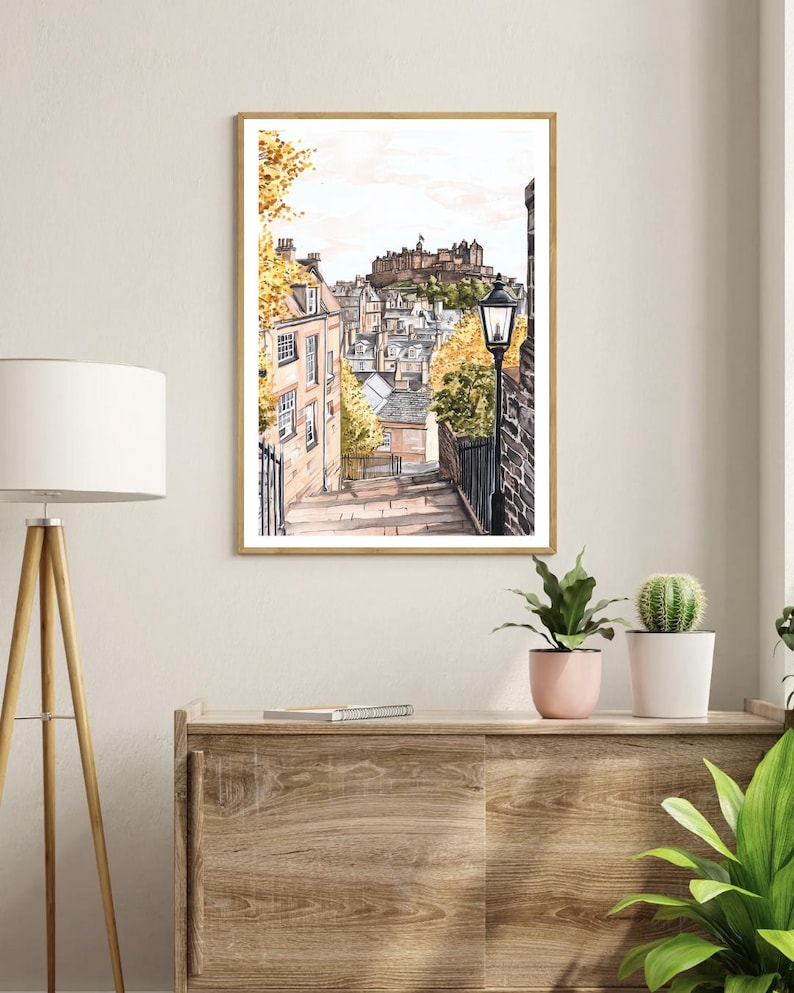May include: A watercolour painting of a street in Edinburgh, Scotland. The street is lined with buildings and there is a castle in the background. The street is cobbled and there is a lamppost on the right side of the image.
