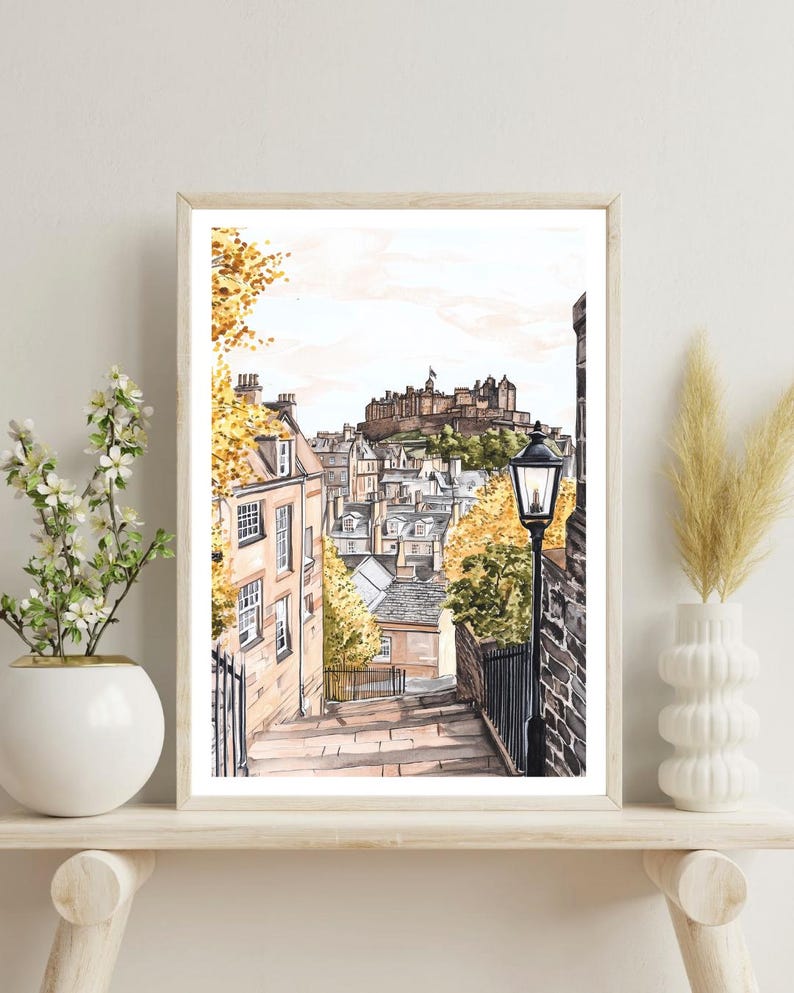 May include: A watercolour painting of a street scene in Edinburgh, Scotland. The painting shows a narrow street with stone steps leading up to a hilltop castle. The castle is in the background, and there are buildings on either side of the street. There is a street lamp on the right side of the street.