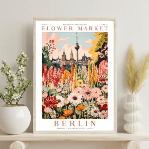 May include: A vintage-style poster advertising a flower market in Berlin, Germany. The poster features a colourful illustration of a flower garden with the Berlin TV Tower in the background. The text on the poster reads "Flower Market, Berlin, Monday - Saturday 09:00 - 19:00".