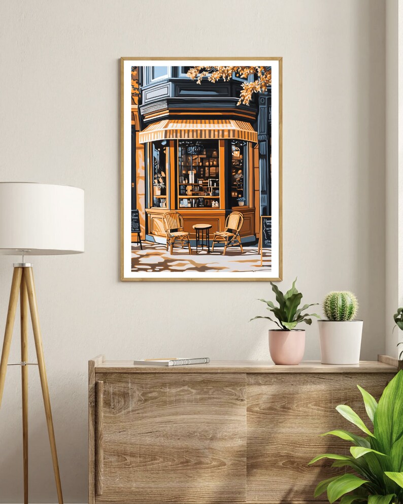 Op de afbeelding: Een schilderij van een winkelgevel met een gele luifel en twee stoelen en een tafel ervoor. De winkelgevel heeft een groot raam met een etalage van goederen erin. Het gebouw is geschilderd in tinten blauw en geel.