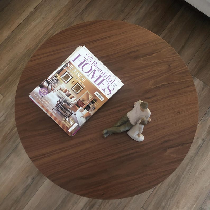 Pu&ograve; includere: Un tavolino da caff&egrave; rotondo in legno con una rivista intitolata "25 Beautiful Homes" e una piccola statuina di una persona seduta sul tavolo.