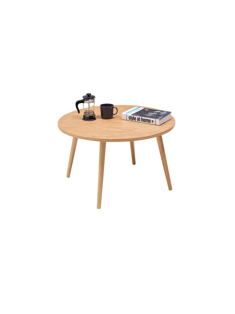 Pu&ograve; includere: Un tavolo rotondo in legno con quattro gambe. Una tazza da caff&egrave; nera e una french press di vetro sono sul tavolo, insieme a un libro intitolato "style at home".