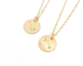 May include: Two gold-colored necklaces with delicate chains. Each necklace features a round pendant with a constellation design and a star. The pendants are approximately 0.5 inches in diameter. The background is white.