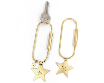 May include: Two gold keychains with star-shaped charms. Each star has a constellation design engraved on it. The keychains are attached to a silver key.