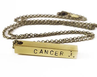 May include: A gold necklace with a bar pendant that says "CANCER" and has the Cancer zodiac symbol.