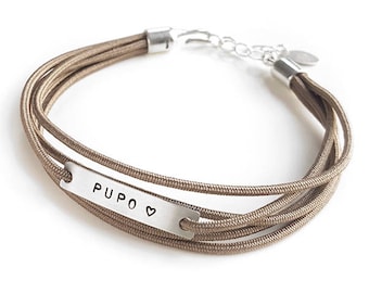 May include: A brown multi-strand bracelet with a silver bar charm engraved with the word "PUPO" and a small heart.