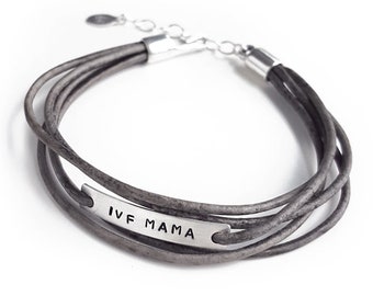 May include: A gray leather wrap bracelet with a silver bar that reads "IVF MAMA".