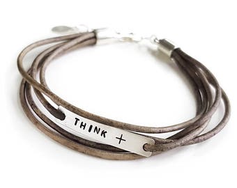 May include: A brown leather wrap bracelet with a silver charm that says "THINK +"
