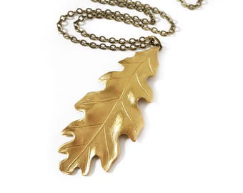 May include: A gold-toned necklace with a large, detailed oak leaf pendant. The chain is a simple, linked style.