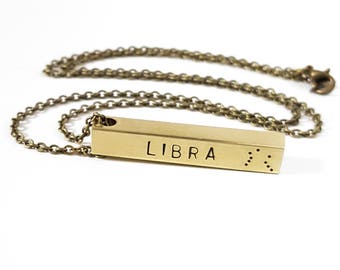 May include: Gold bar necklace with the word "LIBRA" and the Libra zodiac symbol engraved on it.