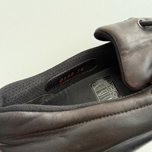 Puede incluir: Primer plano de un zapato de cuero marr&oacute;n. El interior del zapato revela un forro de malla negra y una etiqueta con los n&uacute;meros "0135 36". El zapato tiene un exterior marr&oacute;n oscuro y una suela negra.