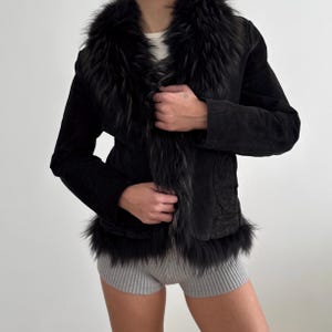 May include: Black suede jacket with a faux fur collar and trim. The jacket has a tailored fit and features a button closure. The faux fur trim adds a touch of luxury to this stylish outerwear piece.