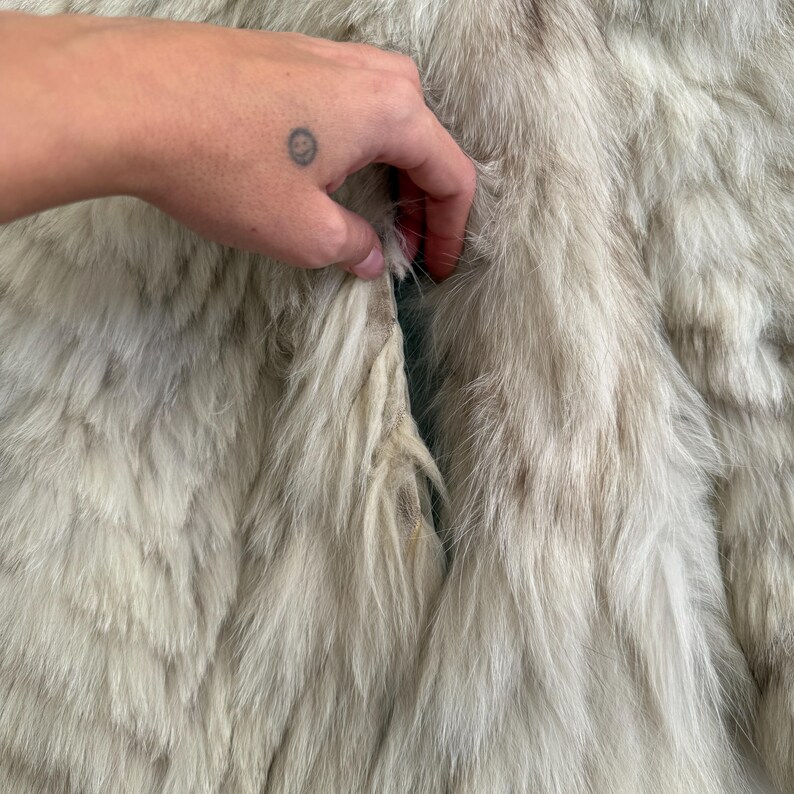 Pu&ograve; includere: Primo piano di un cappotto di pelliccia colorata. La pelliccia &egrave; un mix di bianco e marrone chiaro, con fili lunghi e morbidi. Il cappotto sembra essere vintage o usato, con qualche segno di usura visibile. La consistenza della pelliccia &egrave; evidente, creando una sensazione lussuosa.
