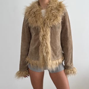 May include: A brown suede jacket with a faux fur collar, trim, and cuffs. The jacket has a classic design with a button-up front. The faux fur is a light tan color, contrasting with the darker brown suede. A stylish outerwear piece.