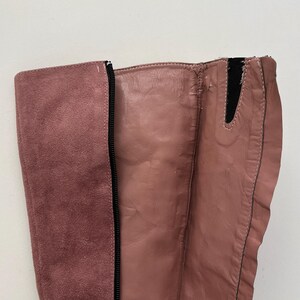 May include: Close-up of a dusty rose-colored boot. The boot features a suede panel on the side and a leather-like material on the front. A black zipper runs along the side of the boot.