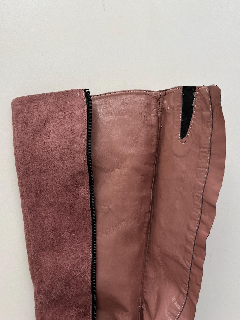 May include: Close-up of a dusty rose-colored boot. The boot features a suede panel on the side and a leather-like material on the front. A black zipper runs along the side of the boot.