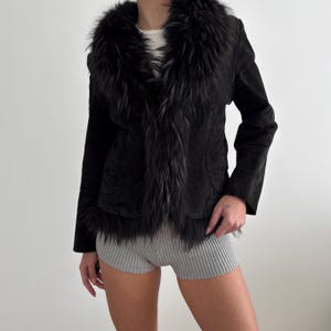 May include: Black suede jacket featuring a faux fur collar and trim. The jacket has a tailored fit with long sleeves. The faux fur trim adds a touch of luxury. A stylish outerwear piece for a chic look. The jacket is a classic design.
