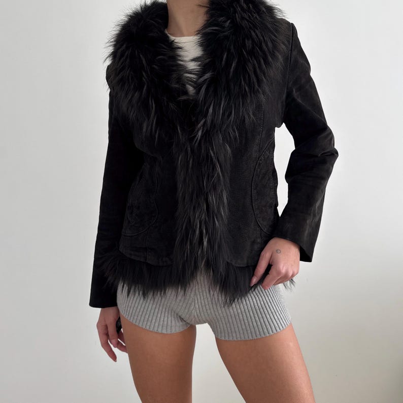 May include: Black suede jacket featuring a faux fur collar and trim. The jacket has a tailored fit with long sleeves. The faux fur trim adds a touch of luxury. A stylish outerwear piece for a chic look. The jacket is a classic design.