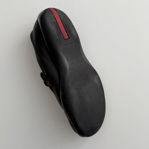 Puede incluir: Zapato de cuero negro con suela texturizada y detalle de raya roja en el tal&oacute;n. El zapato tiene punta redondeada y detalle de correa. La suela es de material duradero.