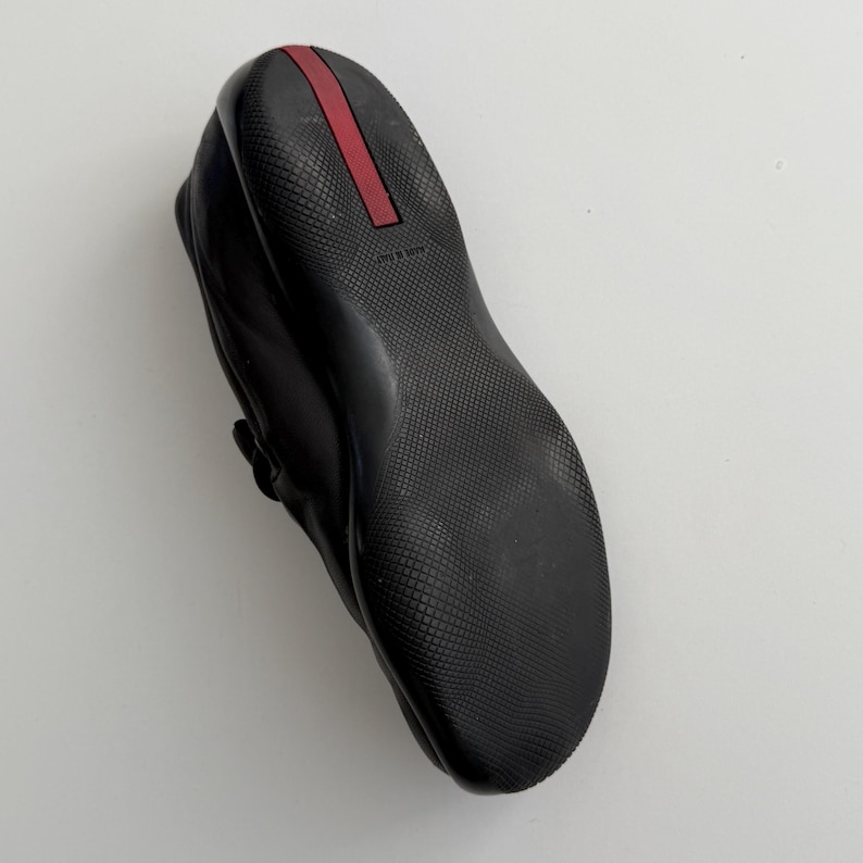 Puede incluir: Zapato de cuero negro con suela texturizada y detalle de raya roja en el tal&oacute;n. El zapato tiene punta redondeada y detalle de correa. La suela es de material duradero.