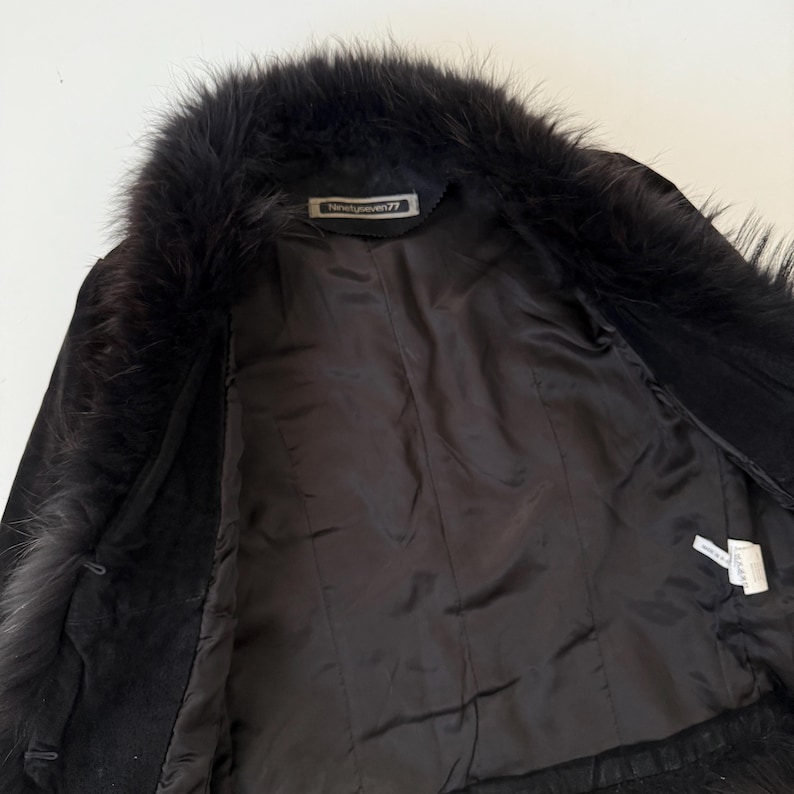 May include: Black suede jacket with a faux fur collar. The jacket has a satin lining and the label reads "Ninetyseven77". The jacket is open, showing the interior details.