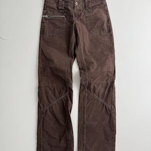 May include: Brown pants featuring a front zipper closure, a button at the waist, and two front pockets. One pocket includes a horizontal zipper detail. The pants have visible stitching along the legs and a label at the waistband that reads ONLY.