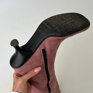May include: A dusty rose-colored suede boot with a black heel and sole. The boot has a zipper running along the side and a size marking of "36" on the sole. The heel is a stiletto style.