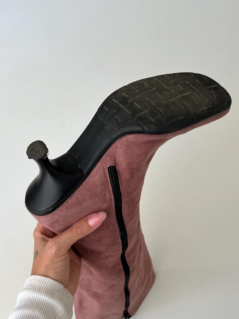 May include: A dusty rose-colored suede boot with a black heel and sole. The boot has a zipper running along the side and a size marking of "36" on the sole. The heel is a stiletto style.