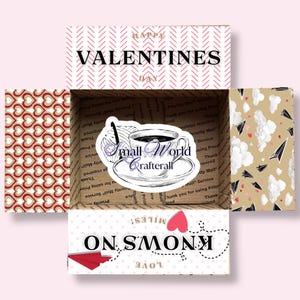 May include: A small, white box with a red and white chevron pattern on the top. The box is open and the inside is lined with brown paper with a pattern of red hearts. The box has a sticker on the inside that says "Small World Crafterall" and a drawing of a cup of coffee. The bottom of the box has a red and white pattern with the words "LOVE KNOWS NO MILES" in black.