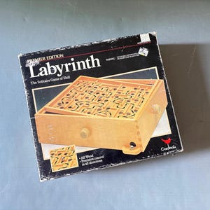 May include: A square black cardboard box for the Labyrinth Premier Edition solitaire game of skill. The box features a graphic of a light-colored wooden maze board with a metal ball, a Cardinal logo, and text including All Wood and Precision control.
