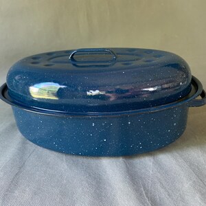 Könnte beinhalten: Eine blaue, gesprenkelte Emaille-Bratpfanne mit passendem Deckel. Die ovale Pfanne hat einen Griff am Deckel und zwei Seitengriffe. Die Pfanne ist zum Kochen und Backen bestimmt.