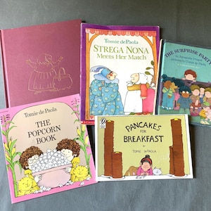 Könnte beinhalten: Eine Sammlung von Kinderbüchern von Tomie dePaola, darunter "Strega Nona Meets Her Match", "The Popcorn Book" und "Pancakes for Breakfast". Die Bücher zeigen farbenfrohe Illustrationen und Text. Die Bücher liegen auf einer grauen Oberfläche.