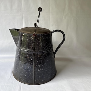 Może przedstawiać: Zabytkowy czajnik do kawy z czarnej emalii z nakrapianym wykończeniem. Czajnik posiada dzióbek, uchwyt i pokrywkę z drucianym uchwytem. Klasyczny artykuł kuchenny, idealny do rustykalnego lub wiejskiego wystroju.