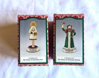 Peut inclure: Deux figurines décoratives de "Un chant de Noël" dans leurs boîtes d'origine. L'une représente une femme en robe blanche, l'autre un homme en robe verte. Les boîtes ont un motif rouge et vert. Le texte est lisible.