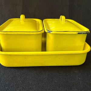 May include: A set of two bright yellow rectangular enamel containers with matching lids, each featuring a small handle on top. The containers are placed inside a matching yellow rectangular enamel tray with rounded corners and a black rim.