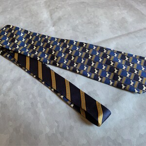 May include: Two neckties with different patterns. One tie features a repeating pattern of white figures on a blue and gold background. The other tie is navy blue with gold stripes and a Greek key design.