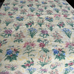 May include: A yellow quilted bedspread with a floral pattern featuring pink, red, blue, and green flowers. The flowers are arranged in a repeating pattern on a yellow background.