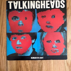 May include: Album cover for Talking Heads' "Remain in Light." The cover features four pixelated faces with red overlays against a blue background. The band's name is in white block letters at the top. The album title is at the bottom.