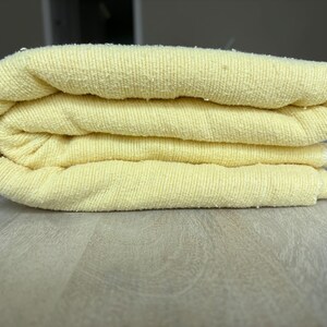 May include: A folded pale yellow towel with a textured, ribbed surface. The fabric has a soft, looped pile construction, showing multiple layers stacked neatly. The light yellow color is consistent across the entire surface of the textile.